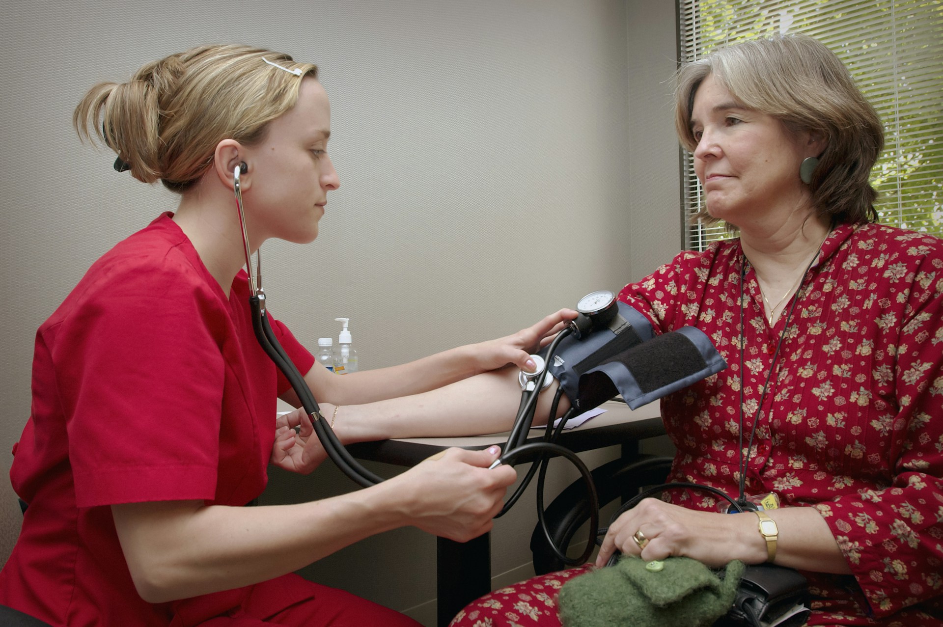 An adult calmly measuring their blood pressure with a digital upper-arm monitor at home.